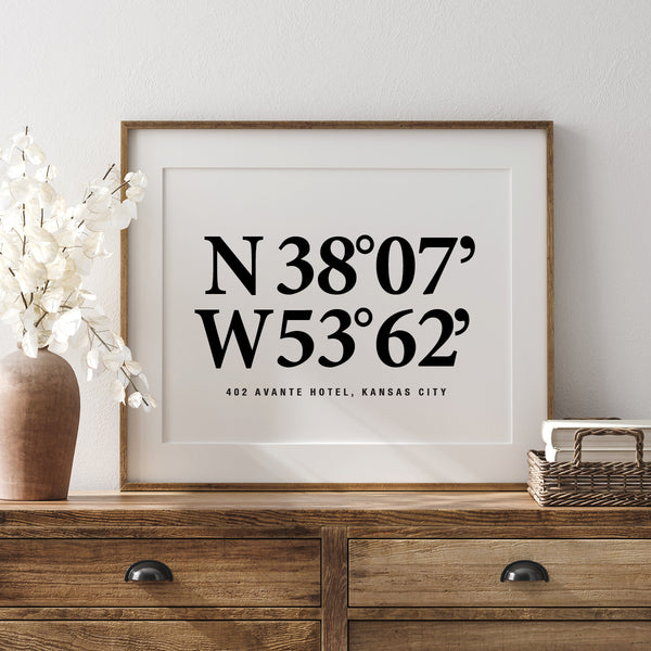 Framed print with coordinates on a wooden dresser with decorative items.